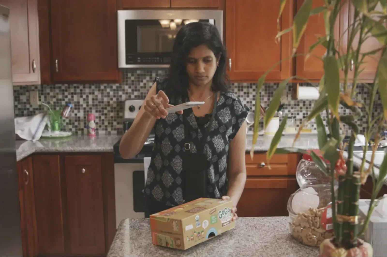 An Indian woman wearing a patterned blouse holds a Pixel above a loaf of bread and uses the Lookout application