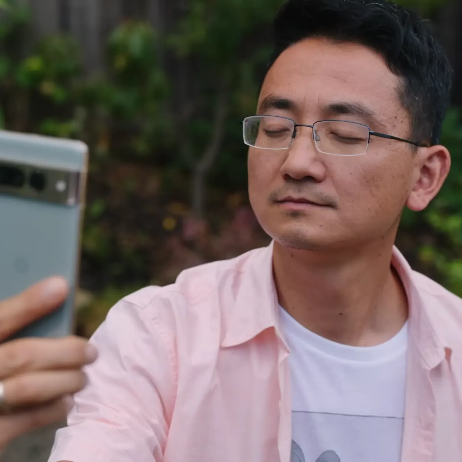 An Asian man with his eyes closed holding up a Pixel phone to take a selfie