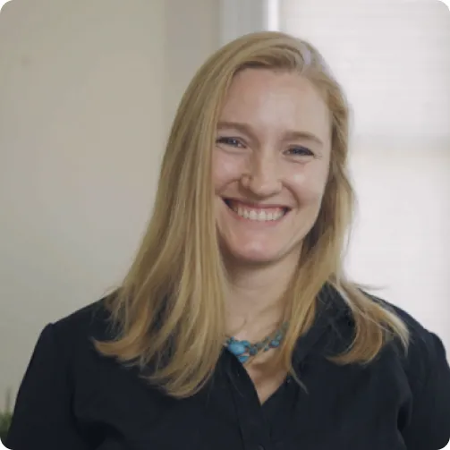 Woman with long blond hair, wearing a black shirt and turquoise necklace is posed smiling